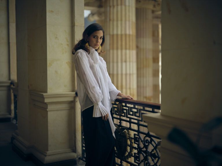 Blusa blanca con lazo y pantalón negro en un balcón del centro de Bogotá, colección Guadalupe de Diego Guarnizo