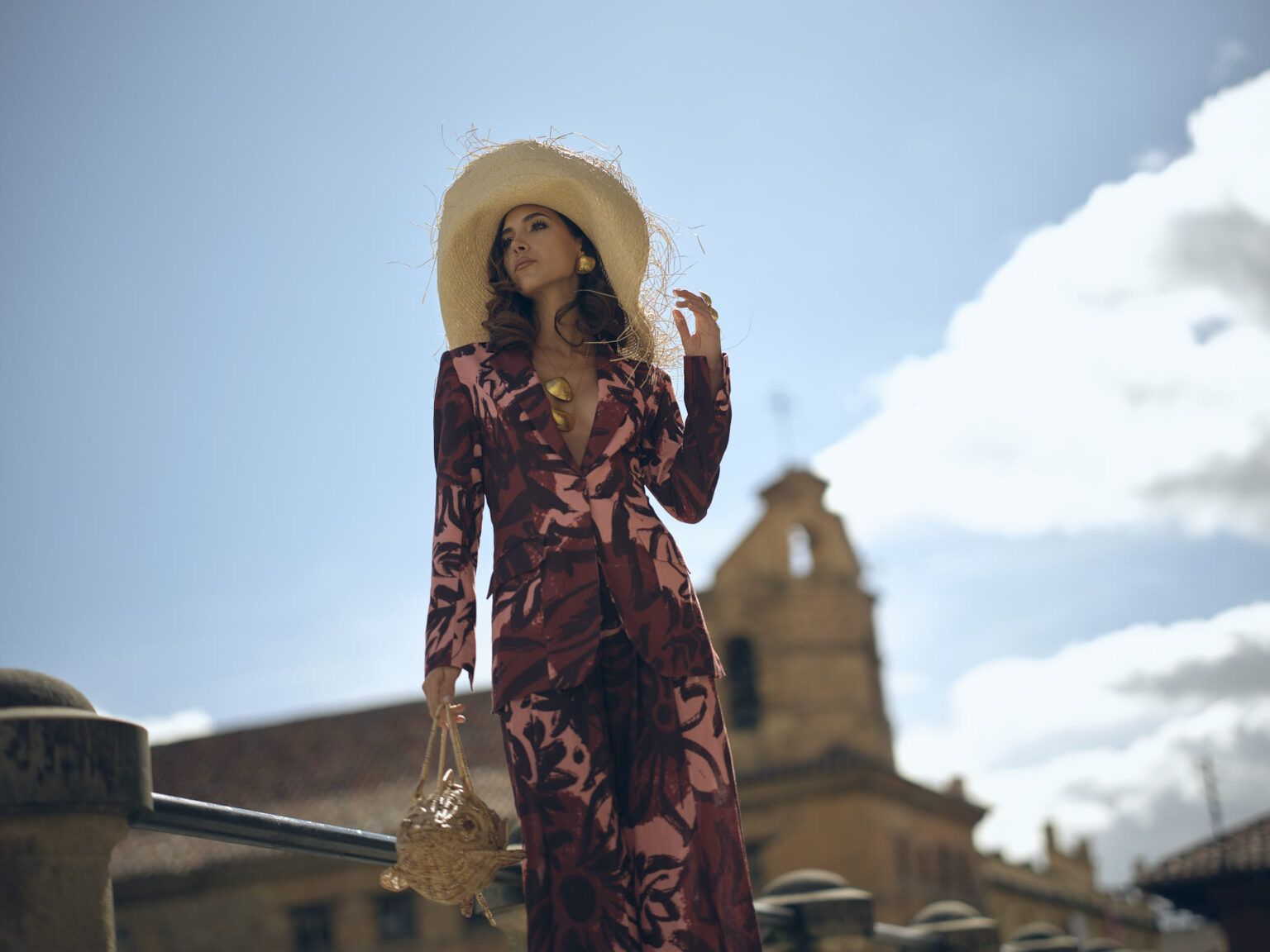 Modelo con sombrero de palma y traje estampado frente a una iglesia del centro de Bogotá, colección Guadalupe de Diego Guarnizo